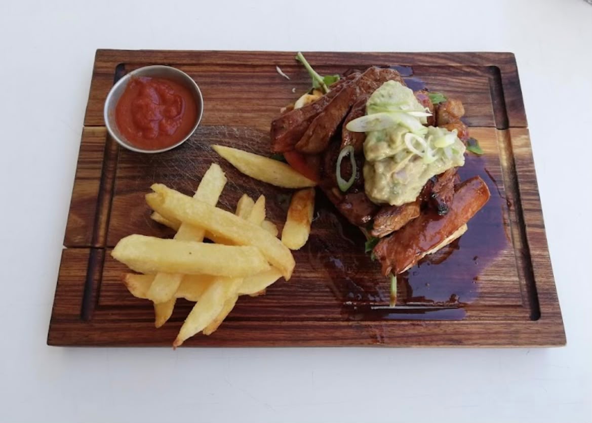 Grilled steak strips with guacamole and chips on a wooden board